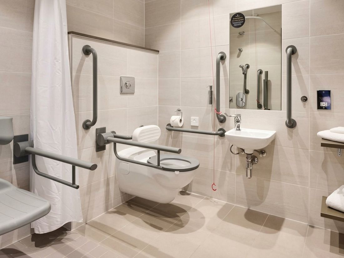Salle de bain adaptée PMR avec barres d'appui, siège de douche et WC suspendu